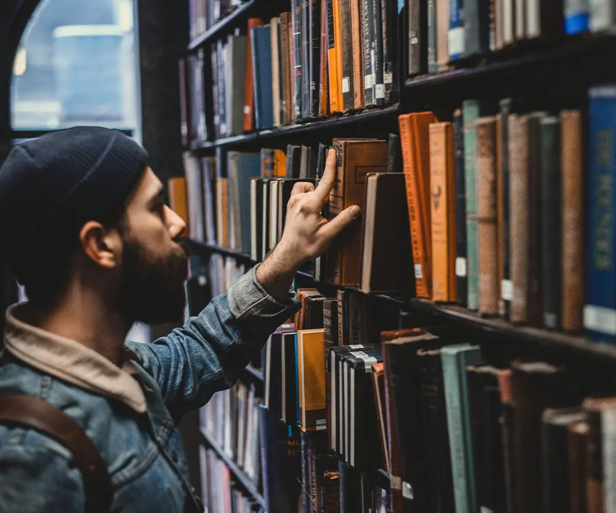 Ein Mann schaut sich verschiedene Bücher in einer Bibliothek an.